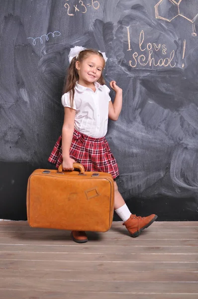 Πορτρέτο του πανέμορφου χαμογελαστή νεαρή πρώτη δημοτικού με κόκκινη βαλίτσα στον μαυροπίνακα φόντο. σχολική και εκπαιδευτική ιδέα — Φωτογραφία Αρχείου