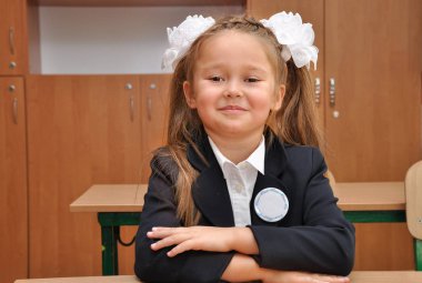 Birinci sınıf öğrencisi okulda bir masada oturuyor. Sınıfta güzel bir kız portresi.