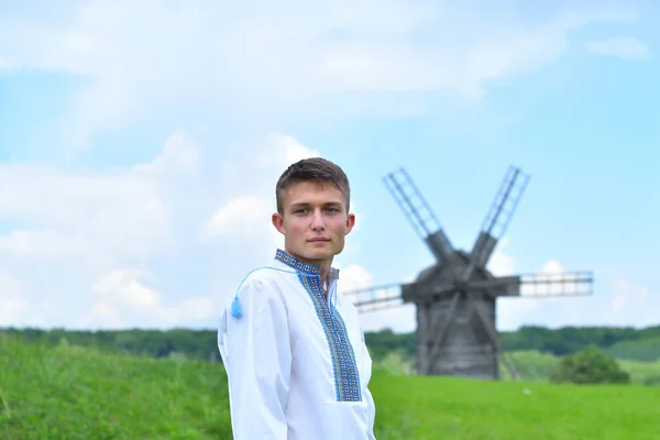 Boy on a green field in traditional embroidered clothes. old mill background — Stock Photo, Image