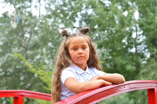 Retrato de una hermosa colegiala joven en el parque de fondo y puente rojo — Foto de Stock