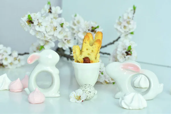 Easter composition on white background.Ceramic rabbit, two eggs and homemade cookies in the form of bunnies.apricot flowers — стоковое фото