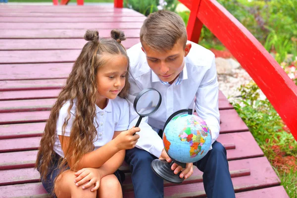 Boy and first-grader girl looking at globe through a magnifying glass . Thoughtful schoolboy and schoolgirl using a magnifying glass .back to school.