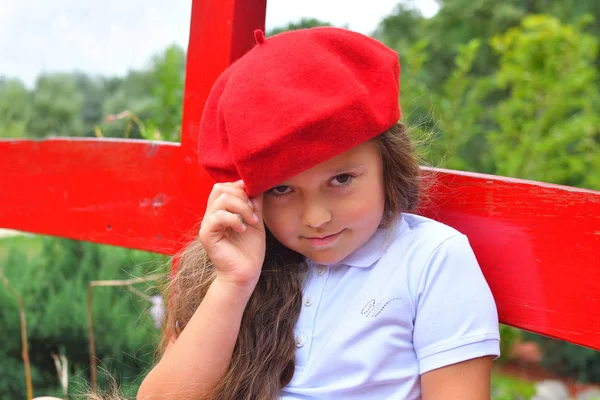 Retrato de una hermosa colegiala en sombrero rojo en el parque de fondo y puente rojo — Foto de Stock