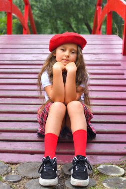 Arka plan parkı ve kırmızı köprü üzerinde kırmızı şapkalı güzel bir genç Schoolgirl Portresi