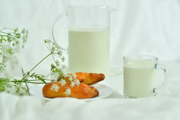 Glazen kruik werper van verse melk met glas en croissant op witte achtergrond. melk concept — Stockfoto