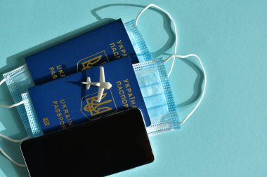 Mavi arka planda Ukrayna pasaportları, tıbbi maskeler ve Amerikan doları. Mavi arka planda seyahat konsepti. COVID-19 ile iptal edilmiş tatil seyahatleri. Covid-19 'un turizm sektörüne etkisi.