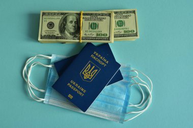 Mavi arka planda Ukrayna pasaportları, tıbbi maskeler ve Amerikan doları. Mavi arka planda seyahat konsepti. COVID-19 ile iptal edilmiş tatil seyahatleri. Covid-19 'un turizm sektörüne etkisi.