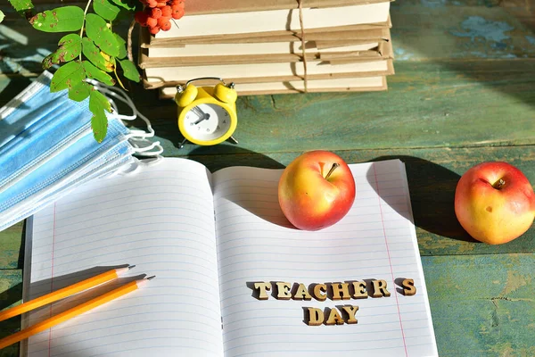 wooden letters teacher\'s day on the notebook.Happy teacher\'s day. books, rowan, apple and medical protective mask with copy space,still life.COVID-19 Distance Online learning concept.Selrctive focus