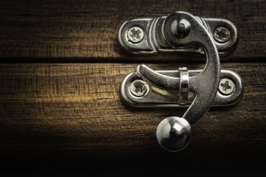 Yatay görüntü formatında cilalı ahşap kutuya takılı gümüş renkli metal sürgülü kilit mandalı bir yakın çekim veya makro görünüm.