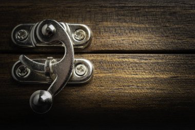 Yatay görüntü formatında cilalı ahşap kutuya takılı gümüş renkli metal sürgülü kilit mandalı bir yakın çekim veya makro görünüm.