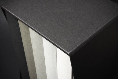 Biraz mezun ve kurnazca dokulu koyu renkli bir arka plan üzerinde siyah sert karton slipcase içinde saklanan beş monokromatik bez bağlı kitap kümesi.