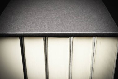 Biraz mezun ve kurnazca dokulu koyu renkli bir arka plan üzerinde siyah sert karton slipcase içinde saklanan beş monokromatik bez bağlı kitap kümesi.