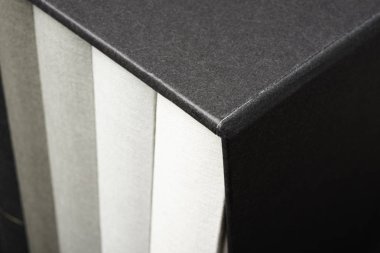 Biraz mezun ve kurnazca dokulu koyu renkli bir arka plan üzerinde siyah sert karton slipcase içinde saklanan beş monokromatik bez bağlı kitap kümesi.