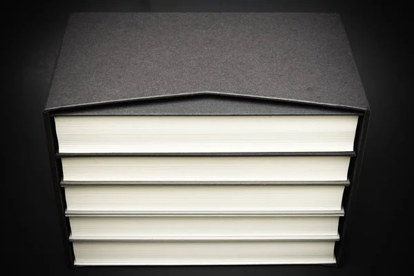 一套五本单色布装书籍 存放在黑色硬纸板滑套内 设置在略带渐变和纹理微妙的深色背景上 — 图库照片
