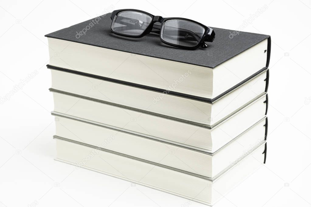 A Neatly Stacked Set Of Five Books With Reading Glasses