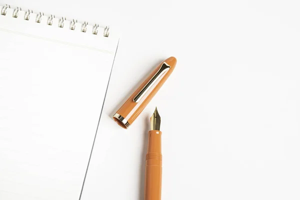 Caneta-tinteiro laranja com caderno espiral — Fotografia de Stock