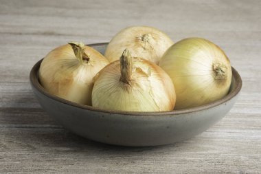 Four freshly harvested sweet white onions set in a ceramic bowl on a rustic wood panel. clipart
