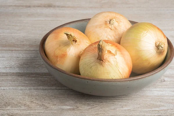 Kırsal bir ahşap panelde seramik bir kasede dört taze toplanmış beyaz soğan..