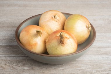 Kırsal bir ahşap panelde seramik bir kasede dört taze toplanmış beyaz soğan..