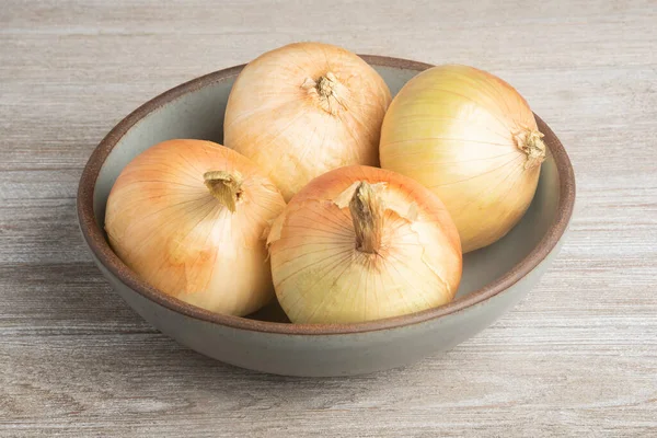 Kırsal bir ahşap panelde seramik bir kasede dört taze toplanmış beyaz soğan..