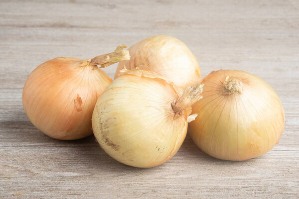 A bunch of four freshly harvested sweet white onions artfully arranged on a white painted rustic wood panel board.
