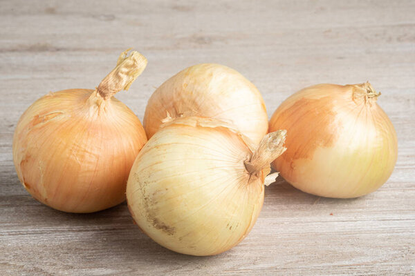 A bunch of four freshly harvested sweet white onions artfully arranged on a white painted rustic wood panel board.