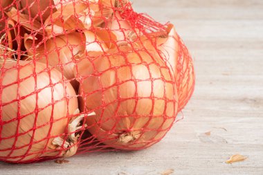 A bunch of onions packaged in a flexible red wire mesh bag for retail sale at groceries and supermarkets. clipart