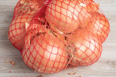 A bunch of onions packaged in a flexible red wire mesh bag for retail sale at groceries and supermarkets. clipart