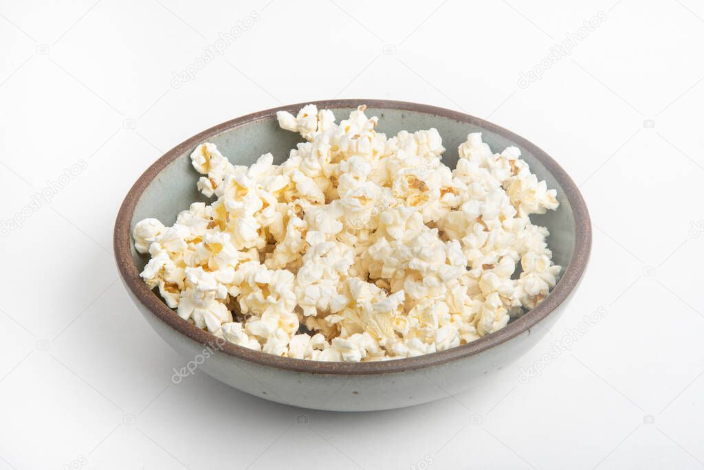 Popcorn in a ceramic bowl set on a plain white background.