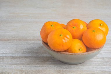 Beyaz desenli ahşap panoda seramik bir kasede bir demet taze portakal..