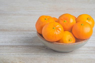 Beyaz desenli ahşap panoda seramik bir kasede bir demet taze portakal..