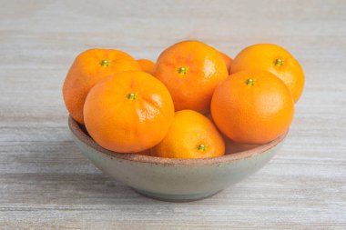 Beyaz desenli ahşap panoda seramik bir kasede bir demet taze portakal..