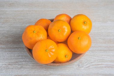 Beyaz desenli ahşap panoda seramik bir kasede bir demet taze portakal..