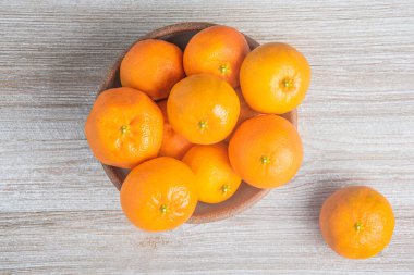 Beyaz desenli ahşap panoda seramik bir kasede bir demet taze portakal..