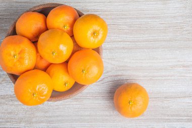 Beyaz desenli ahşap panoda seramik bir kasede bir demet taze portakal..