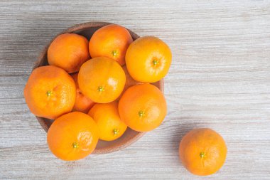 Beyaz desenli ahşap panoda seramik bir kasede bir demet taze portakal..