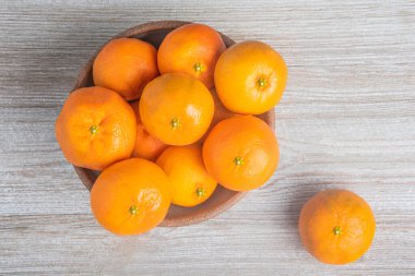 Beyaz desenli ahşap panoda seramik bir kasede bir demet taze portakal..