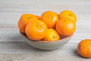 Beyaz desenli ahşap panoda seramik bir kasede bir demet taze portakal..