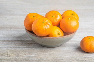 Beyaz desenli ahşap panoda seramik bir kasede bir demet taze portakal..