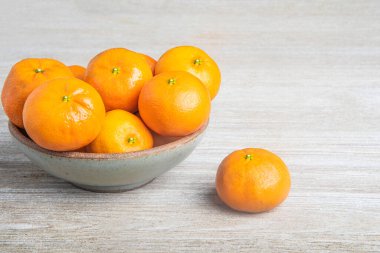 Beyaz desenli ahşap panoda seramik bir kasede bir demet taze portakal..