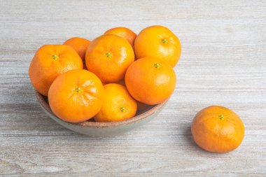 Beyaz desenli ahşap panoda seramik bir kasede bir demet taze portakal..