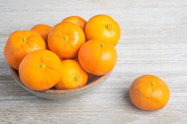 Beyaz desenli ahşap panoda seramik bir kasede bir demet taze portakal..