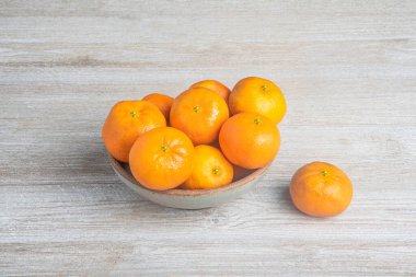 Beyaz desenli ahşap panoda seramik bir kasede bir demet taze portakal..