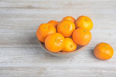 Beyaz desenli ahşap panoda seramik bir kasede bir demet taze portakal..