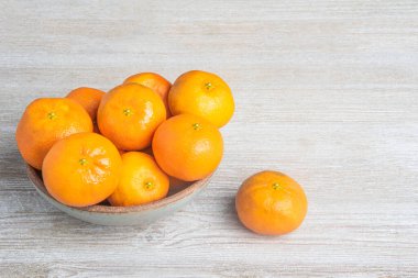 Beyaz desenli ahşap panoda seramik bir kasede bir demet taze portakal..