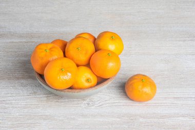 Beyaz desenli ahşap panoda seramik bir kasede bir demet taze portakal..