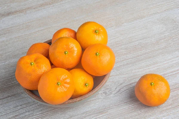 Beyaz desenli ahşap panoda seramik bir kasede bir demet taze portakal..