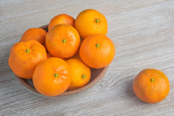 Beyaz desenli ahşap panoda seramik bir kasede bir demet taze portakal..