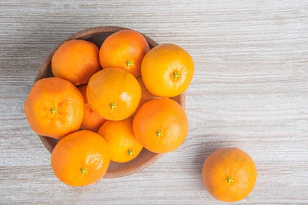 Beyaz desenli ahşap panoda seramik bir kasede bir demet taze portakal..