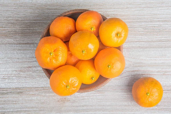 Beyaz desenli ahşap panoda seramik bir kasede bir demet taze portakal..